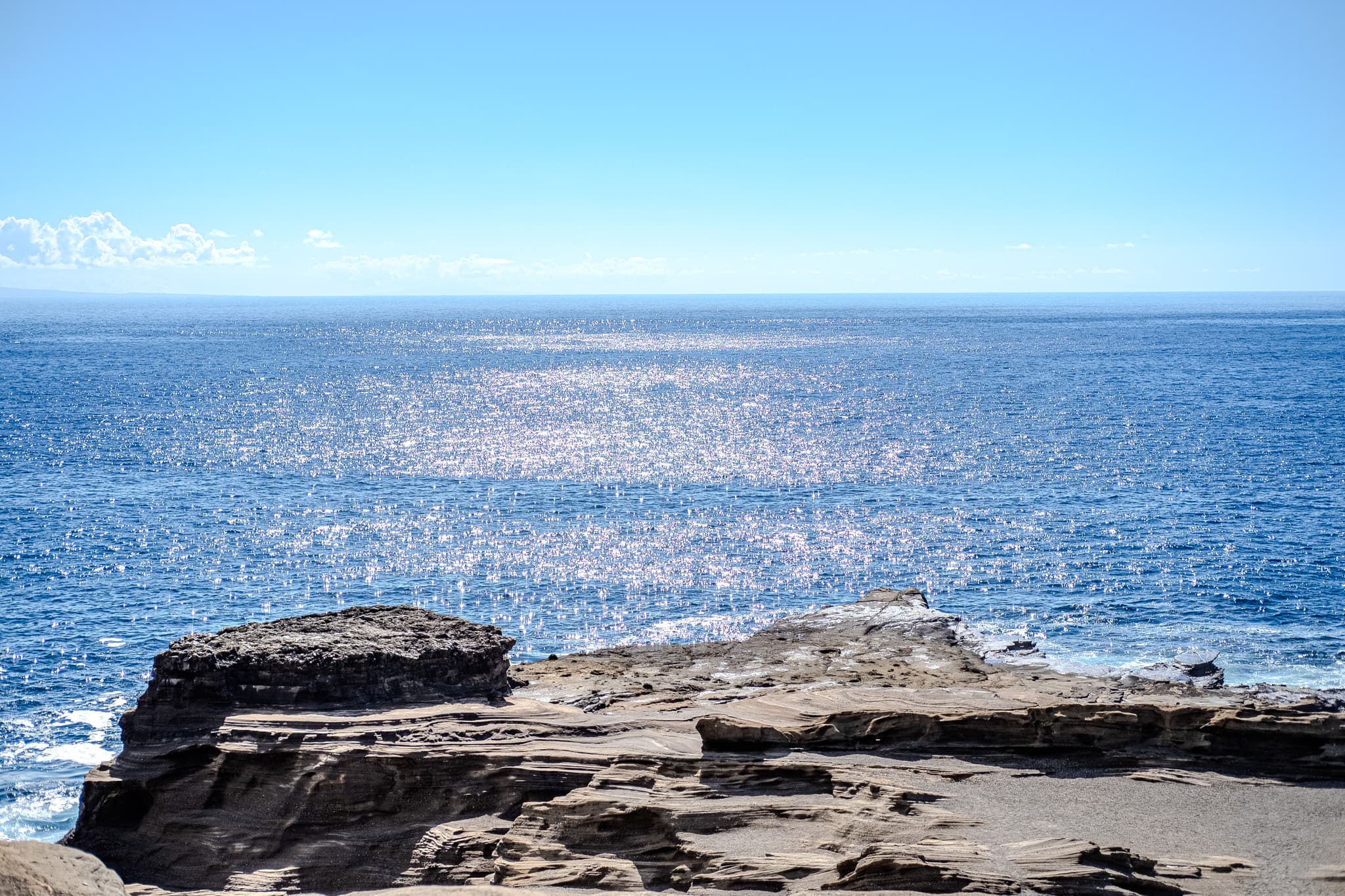 Sunlight glittering on the ocean beyond lava rock