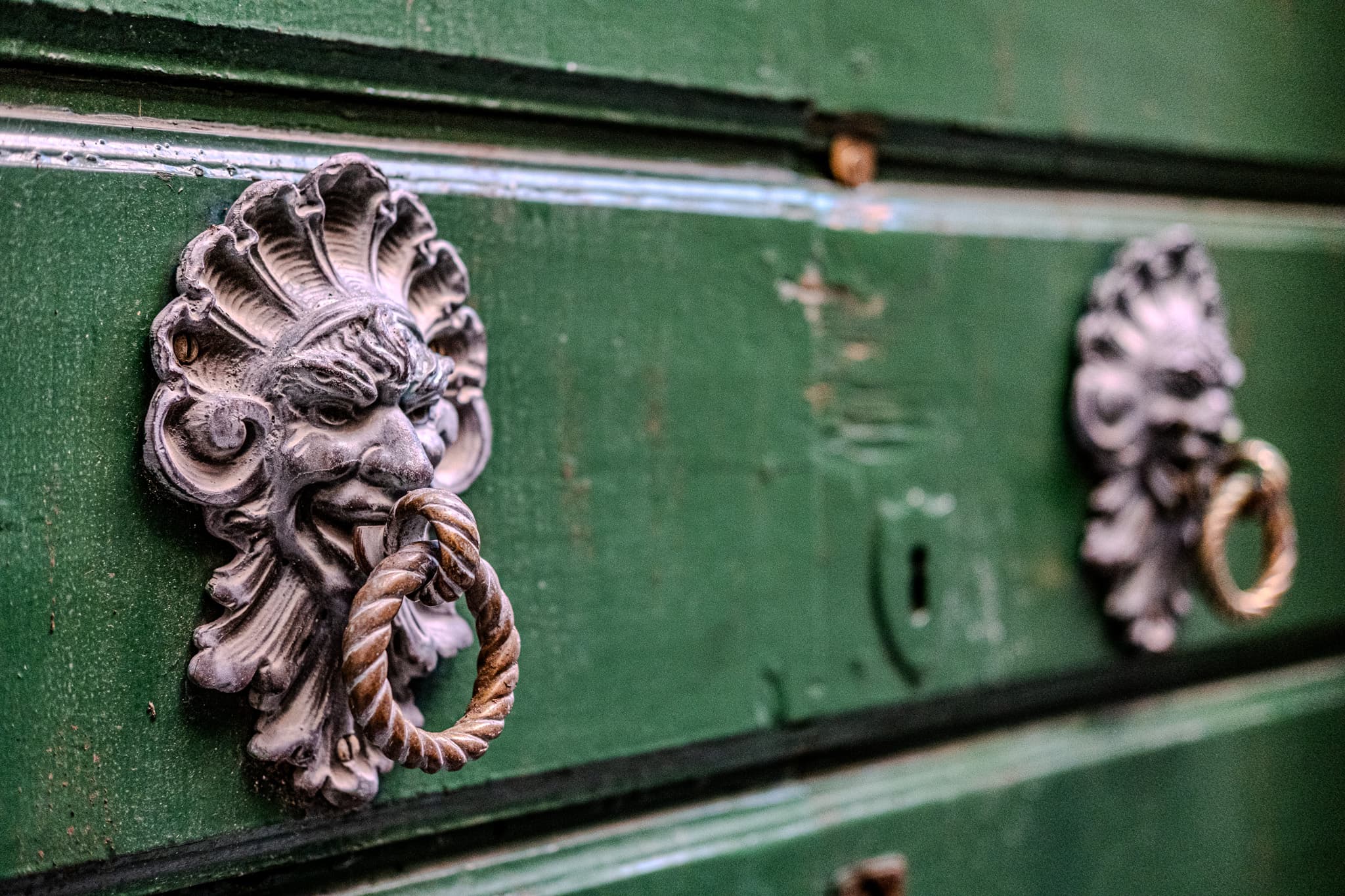Ornate door knockers on a weathered green door