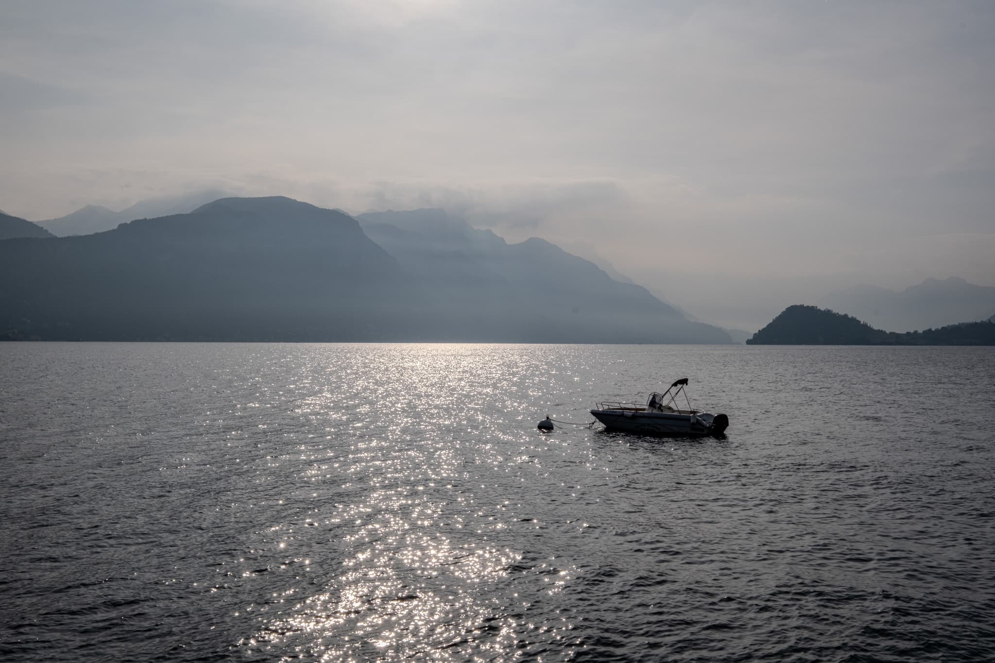 Small boat on glittering water beneath misty mountains