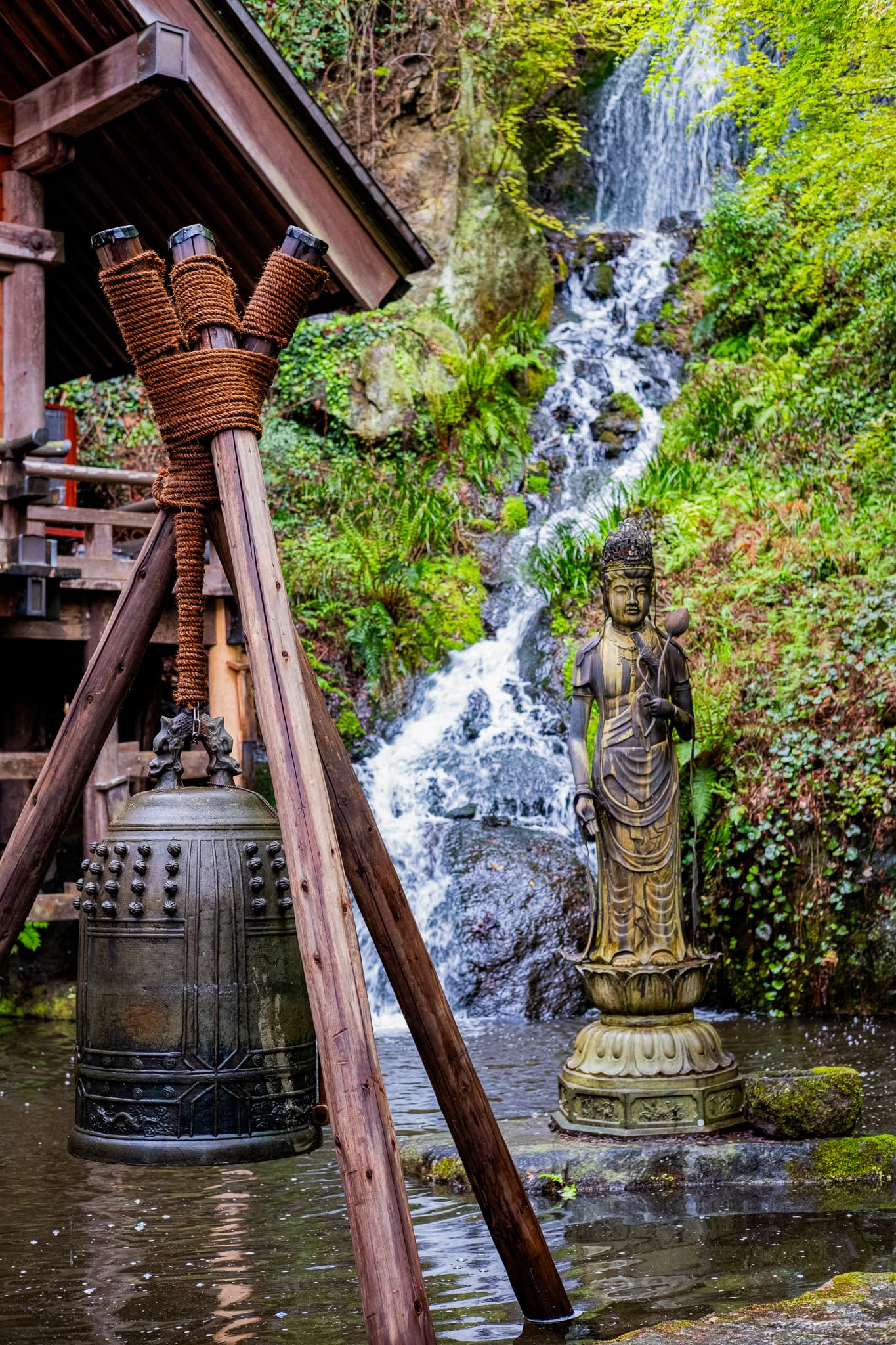 Temple bell and statue beside a waterfall