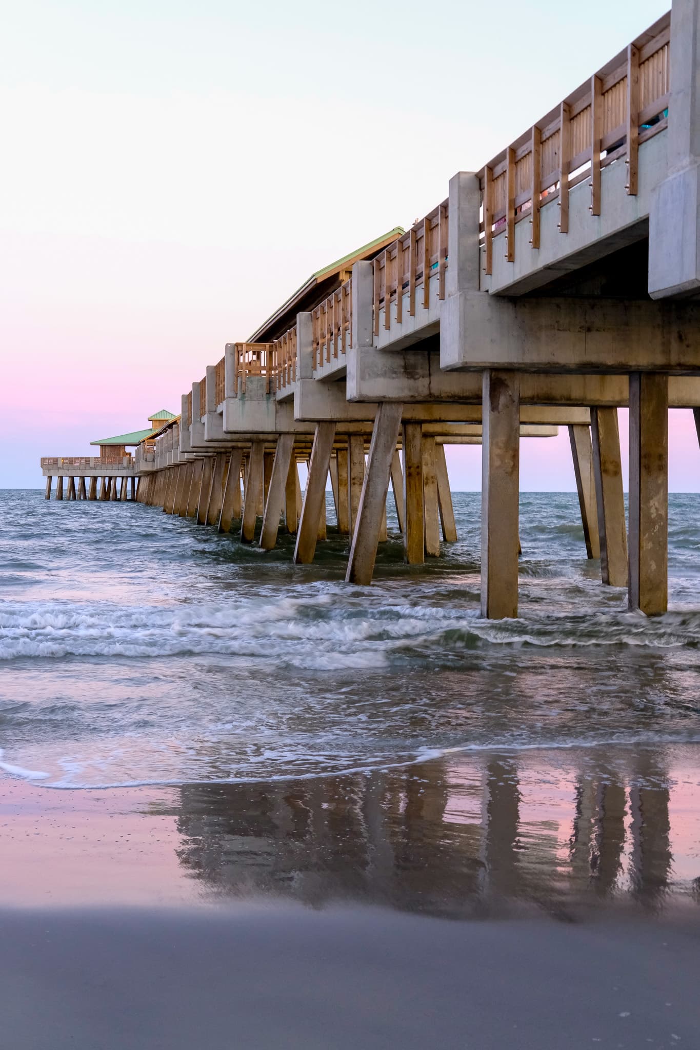 Pier pilings reflected on the wet sand at dusk