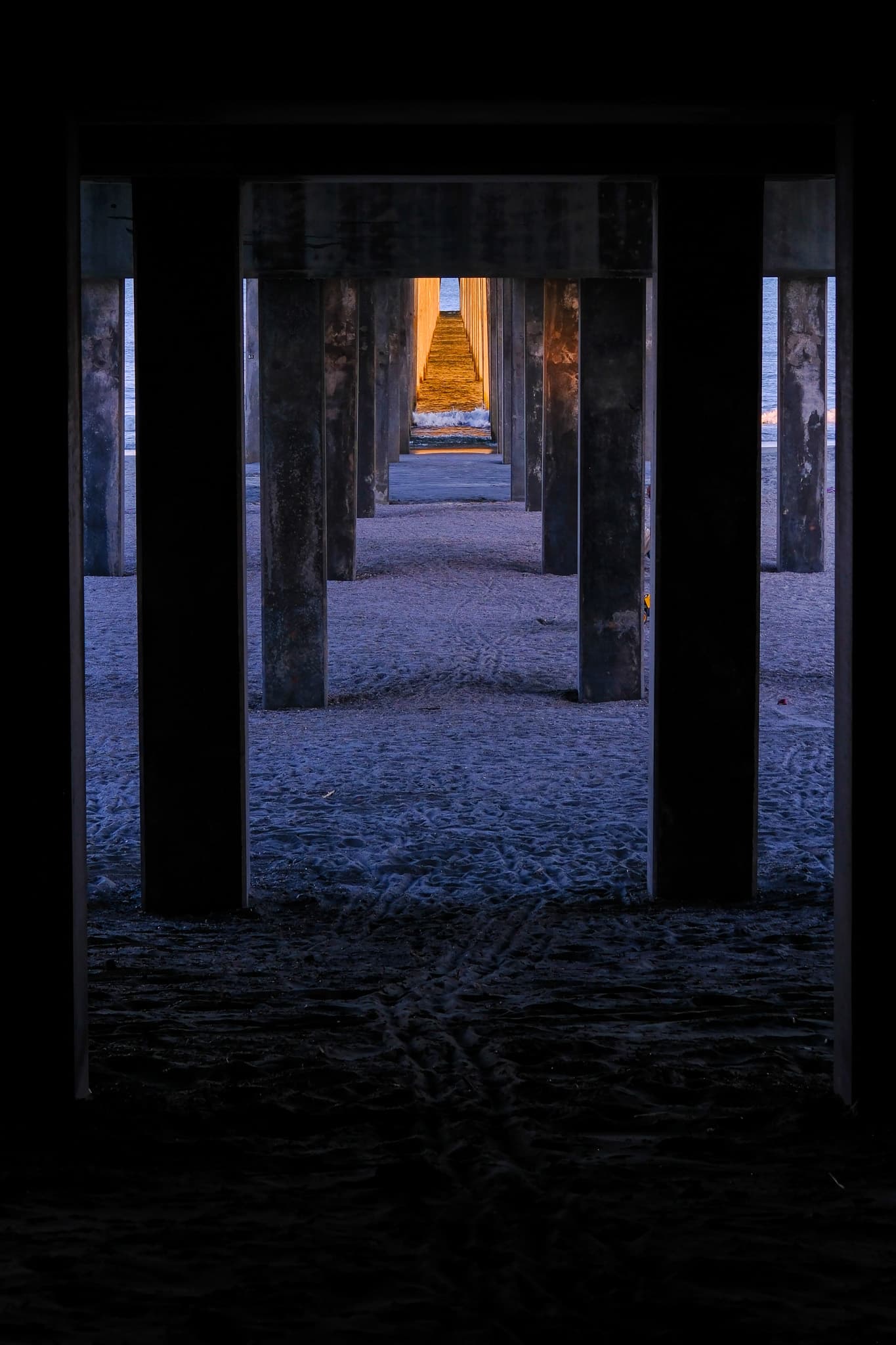 Rows of pillars beneath the pier with light at the far end